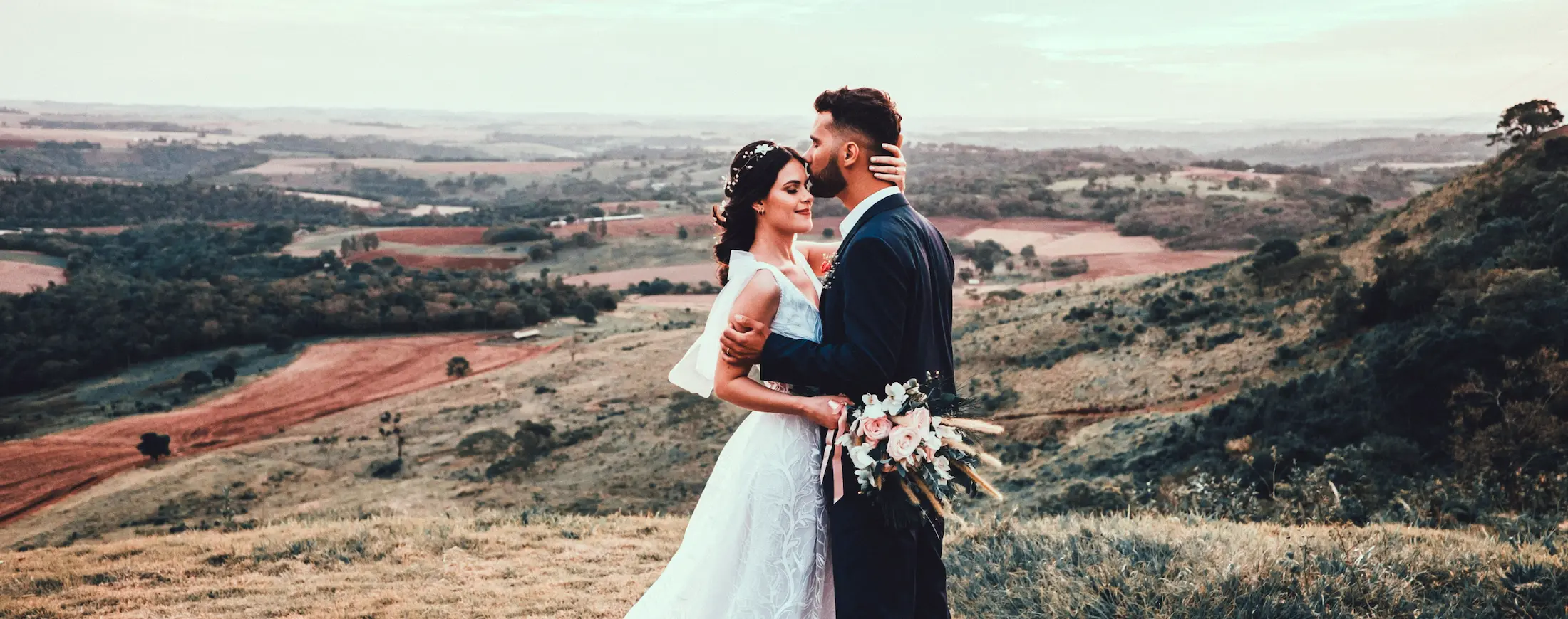 Bride and groom embracing on a scenic hilltop during their wedding photoshoot.