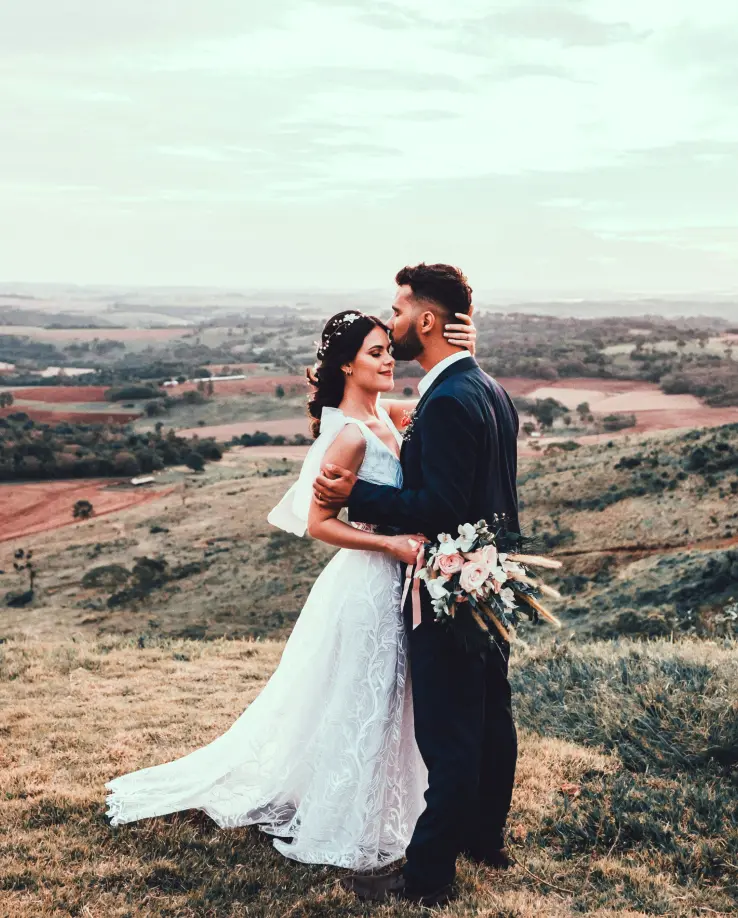 Bride and groom embracing on a hill with scenic rural background.