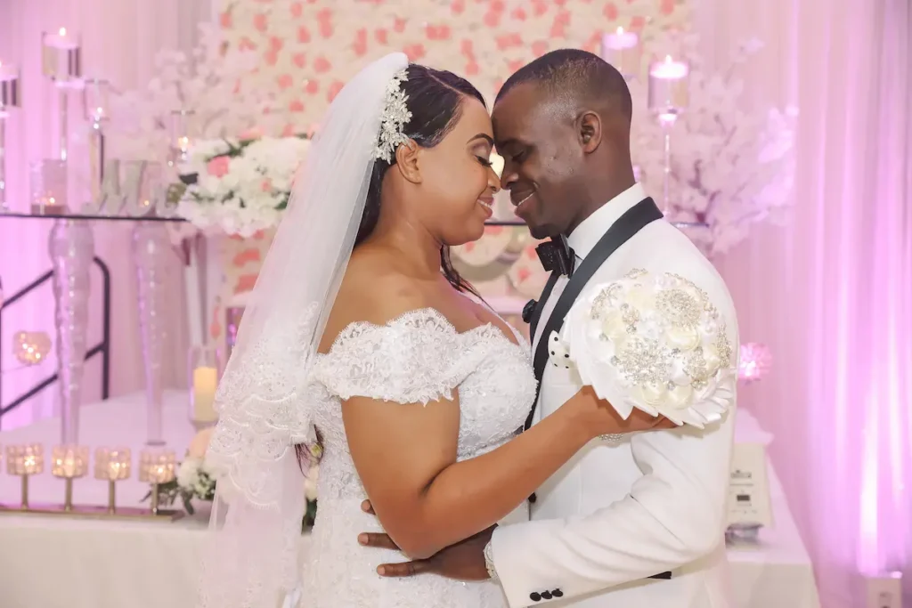 Bride and groom embracing in a white and pink-themed wedding venue.